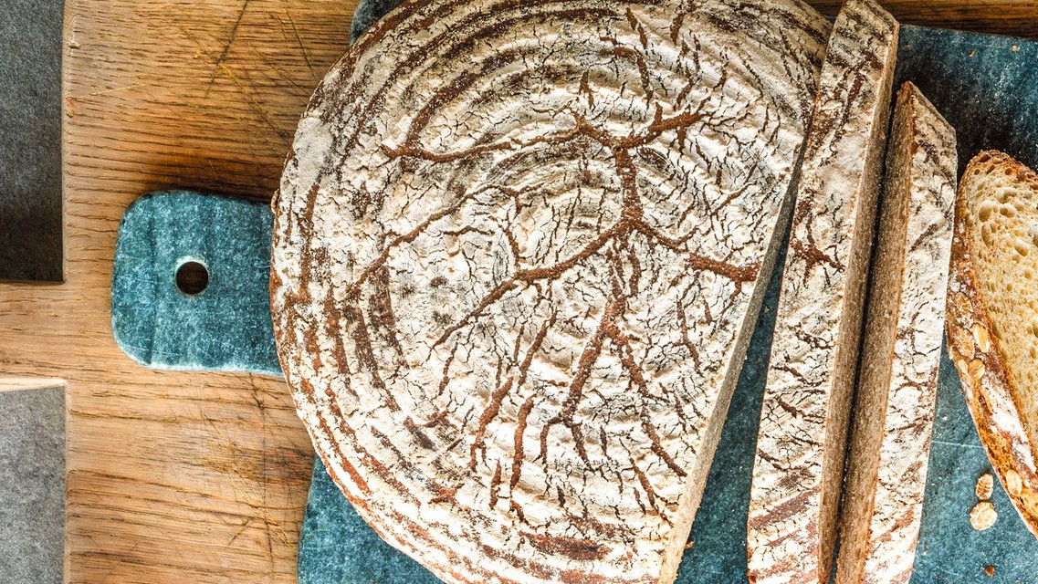 Angeschnittenes Dinkelflockenbrot auf einem Holzbrett mit Marmorplatte